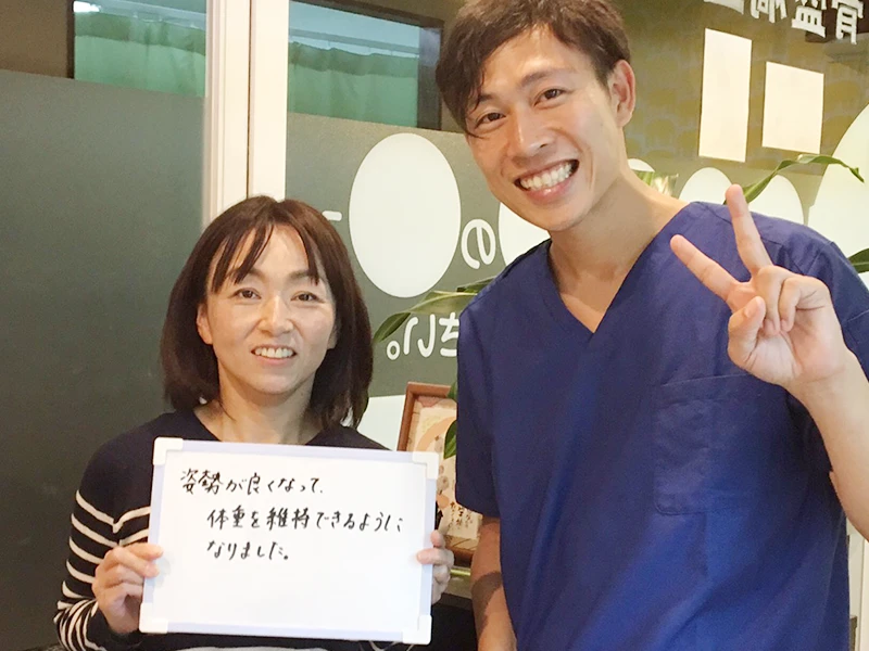 ご来院いただいた方と院長の写真。ボードに「姿勢が良くなって、体重を維持できるようになりました」